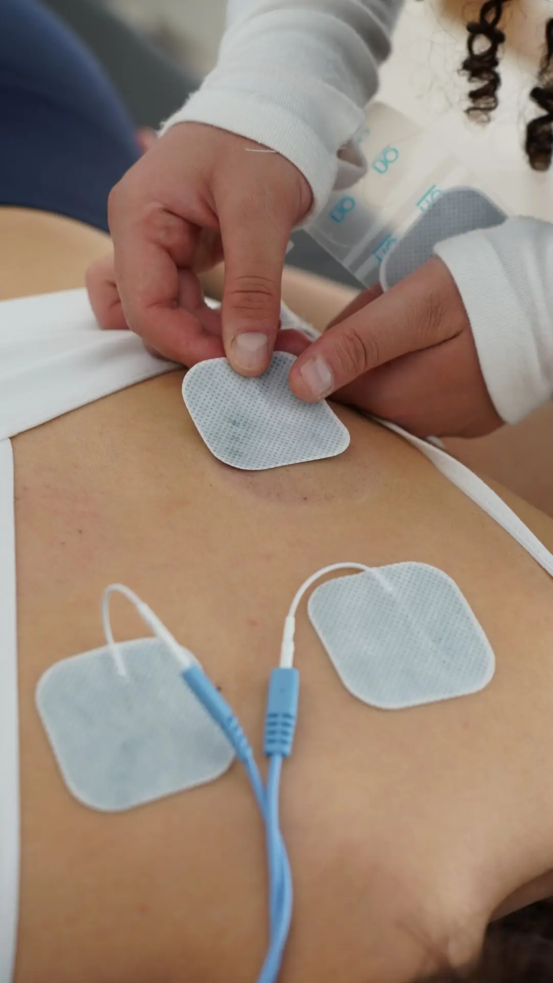 Hands applying electrotherapy pads on the back for muscle stimulation.